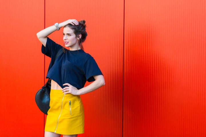 Junge modebewusste Frau trägt ein dunkelblaues T-Shirt mit einem gelben Rock. Dieser Look nennt sich Colour Blocking.
