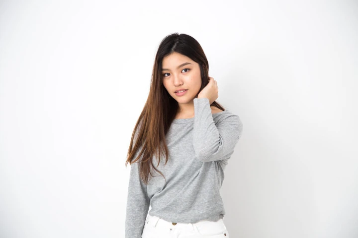Asiatische Frau steht vor einem weißen Hintergrund und trägt ein graues Langarmshirt.