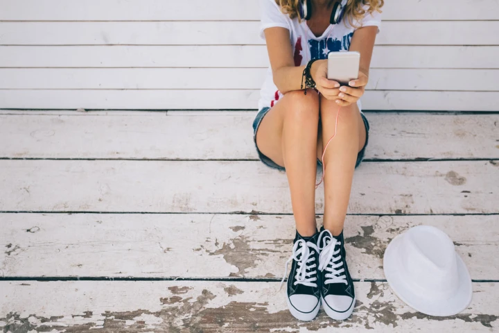 Frau trägt Chucks mit Handy in der Hand