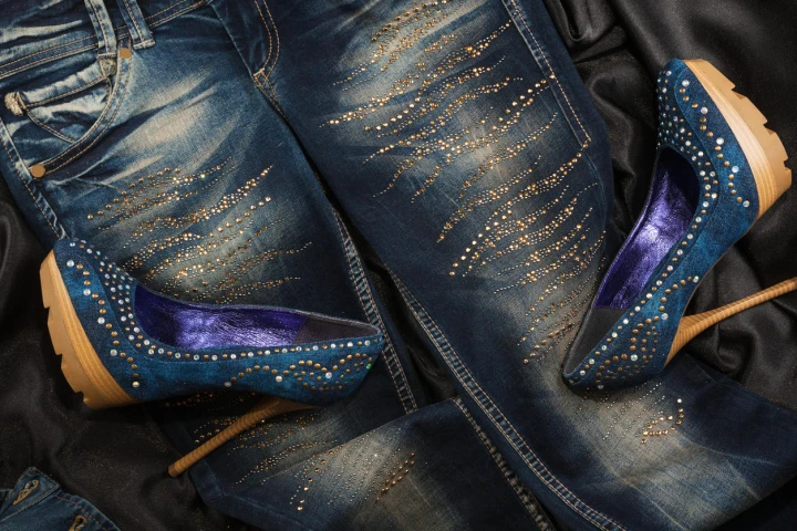 Hier liegen zwei dunkelblaue High Heels auf einer mit Strass verzierten Jeans.