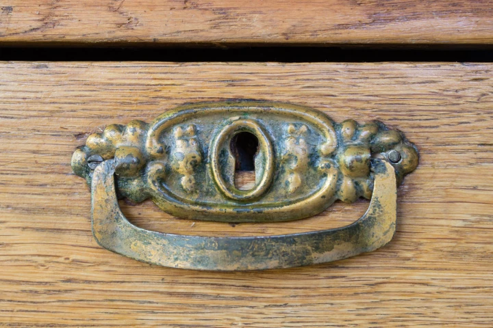 Hier ist ein alter kupferner Möbelgriff zu sehen. Auf dem Möbelgriff hat sich Patina abgesetzt.